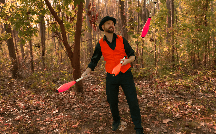 juggler in black and orange costume juggling clubs